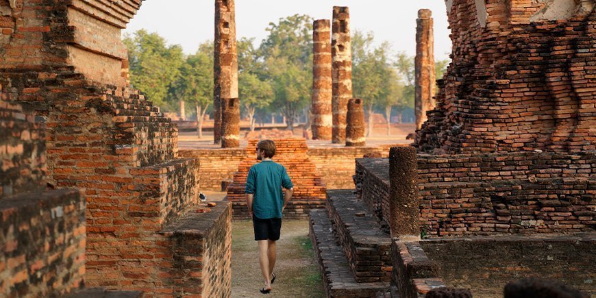 Mann, der bei Sonnenaufgang durch die Ruinen von Sukhothai spaziert