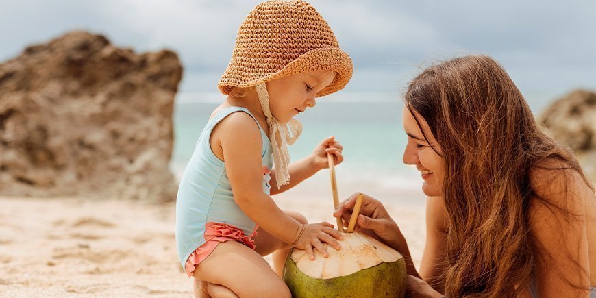 Mutter und Tochter trinken aus einer Kokosnuss an einem Strand in Thailand